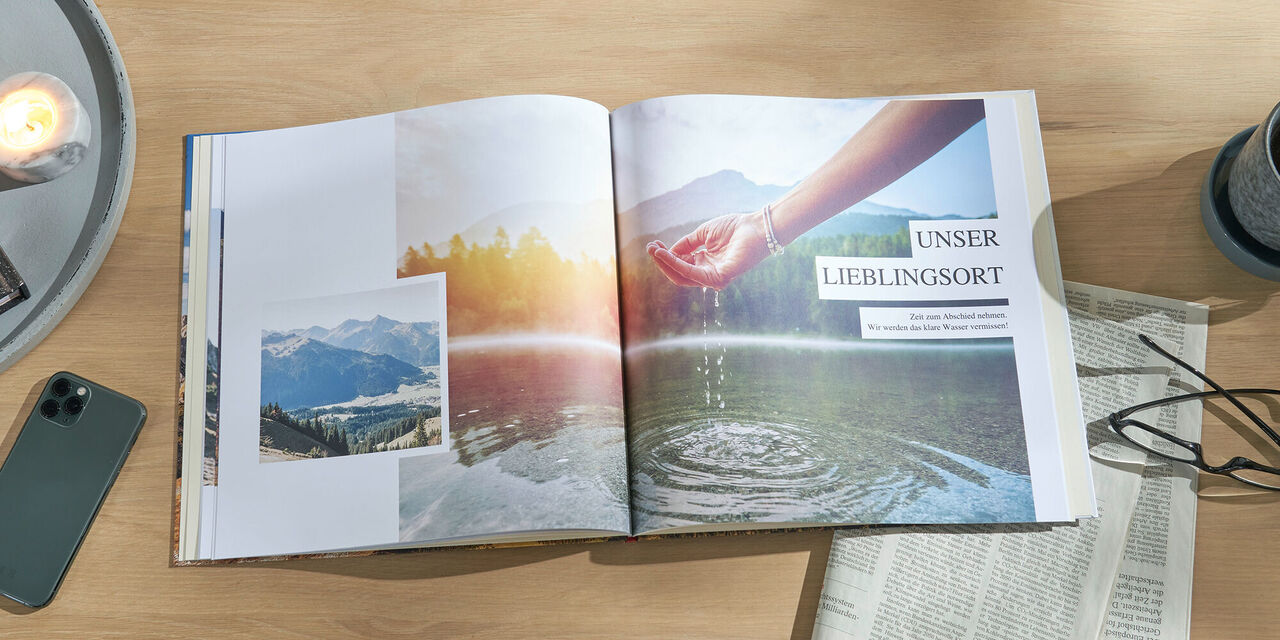 Ein aufgeschlagenes CEWE FOTOBUCH liegt auf einem Tisch. Darin sind mehrere Aufnahmen von der Natur zu sehen sowie die Überschrift „Unser Lieblingsort“. Rechts daneben steht ein Becher mit Tee und es liegen eine Zeitung und eine Brille auf dem Tisch.