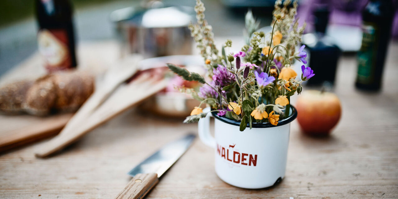 Detailansicht des gedeckten Tisches. Im Fokus liegen ein Messer und eine mit Blumen versehene Tasse.